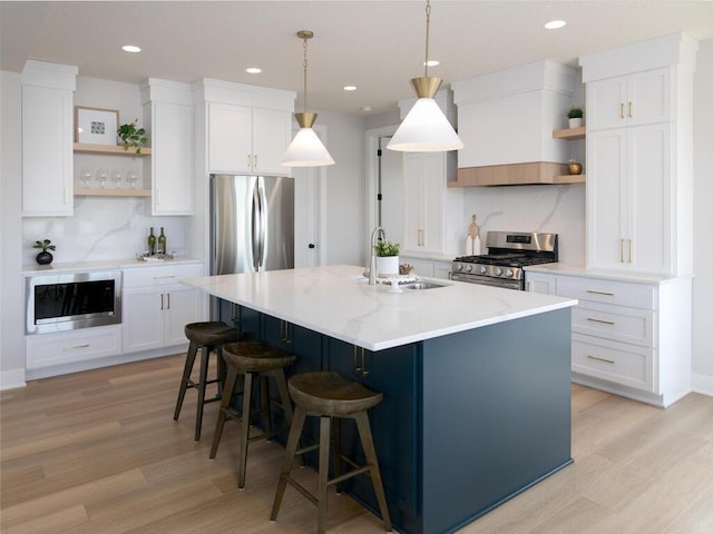 kitchen featuring open shelves, appliances with stainless steel finishes, a kitchen island with sink, and a sink