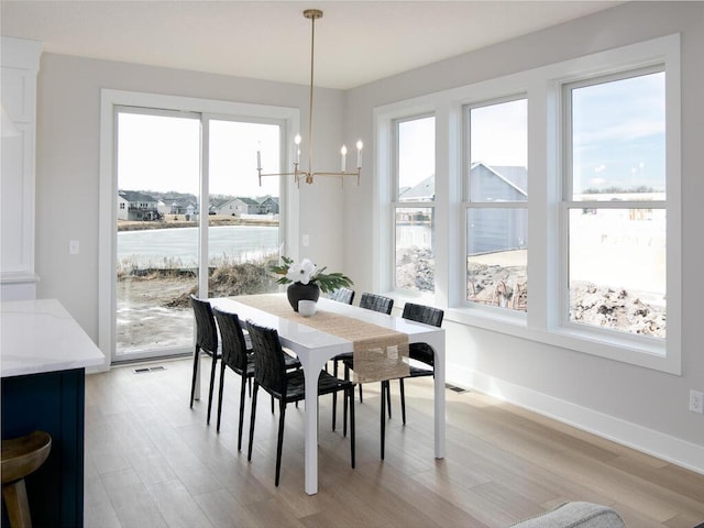 dining area with light wood finished floors, a notable chandelier, visible vents, and baseboards