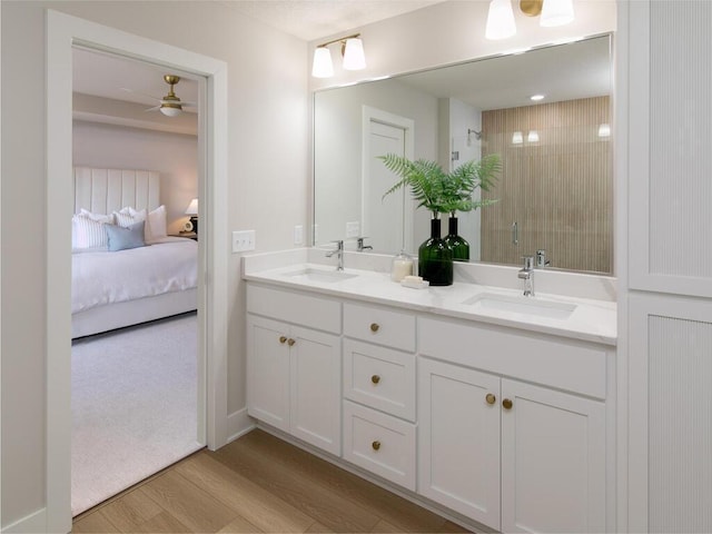 ensuite bathroom featuring a sink, wood finished floors, a stall shower, and double vanity