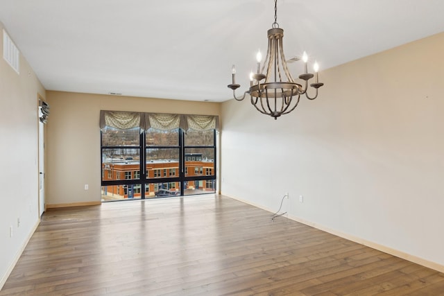 spare room with baseboards, wood finished floors, visible vents, and a notable chandelier