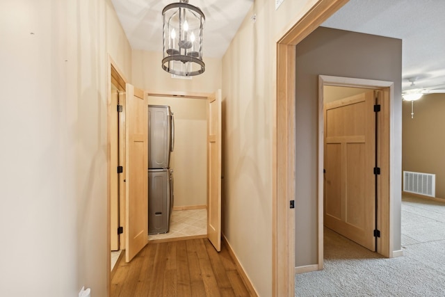 hallway with baseboards, light carpet, visible vents, and an inviting chandelier