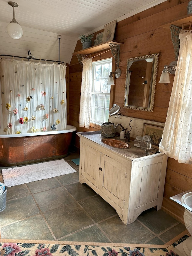 bathroom featuring vanity, wooden walls, vaulted ceiling, and a washtub