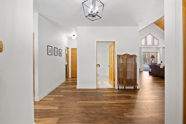 hall with dark hardwood / wood-style flooring, an inviting chandelier, and vaulted ceiling