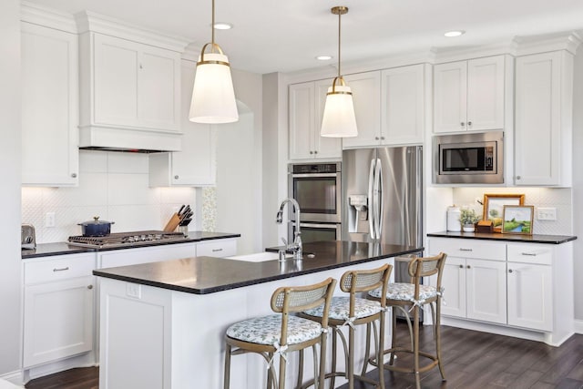 kitchen featuring appliances with stainless steel finishes, dark countertops, white cabinetry, and an island with sink