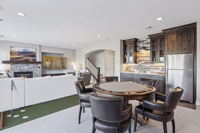 dining room with arched walkways, recessed lighting, a stone fireplace, and stairs