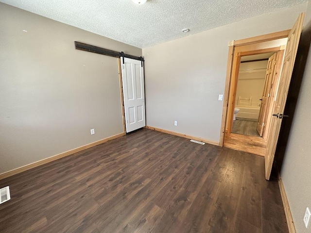 unfurnished bedroom featuring a textured ceiling, a barn door, and dark wood-type flooring