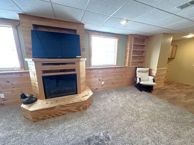 carpeted living room with a paneled ceiling and wood walls