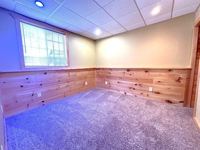 empty room with carpet, a drop ceiling, and wooden walls