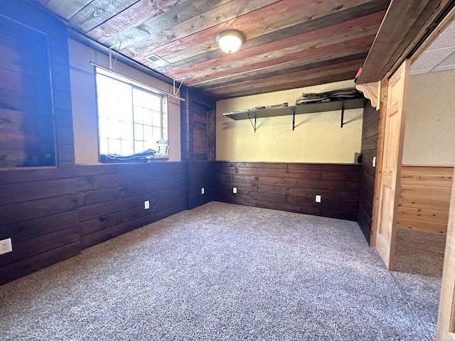 carpeted empty room featuring wooden ceiling and wood walls