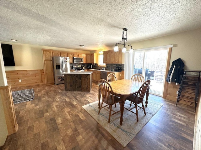 dining space featuring a wainscoted wall, a textured ceiling, wood walls, and dark wood-style flooring