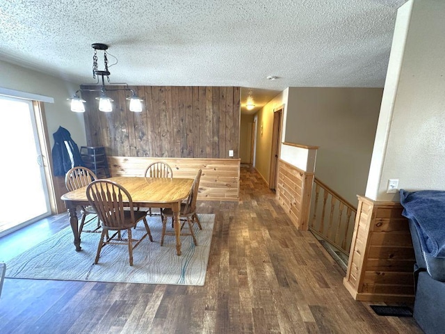 dining space with visible vents, a textured ceiling, wood finished floors, and wooden walls