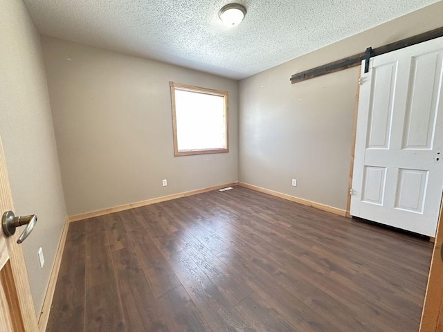 interior space featuring a textured ceiling, visible vents, baseboards, dark wood finished floors, and a barn door
