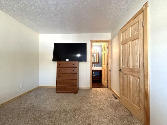 unfurnished bedroom with baseboards, ensuite bath, carpet flooring, and a textured ceiling