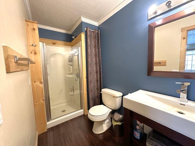 bathroom featuring a textured ceiling, crown molding, a shower stall, wood finished floors, and toilet