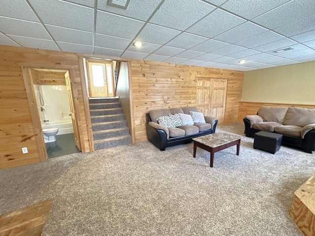 carpeted living room featuring wood walls, a paneled ceiling, and stairway