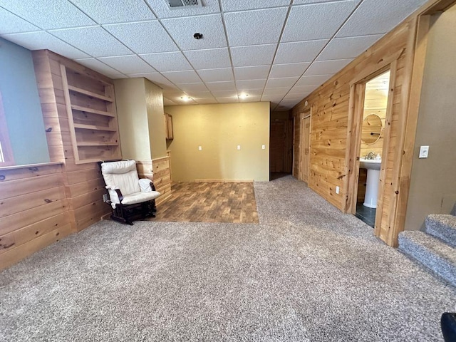 sitting room featuring a drop ceiling, carpet, wooden walls, and visible vents