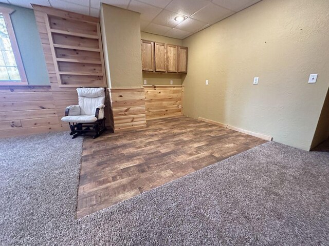 interior space featuring a drop ceiling, carpet flooring, a textured wall, and wood finished floors
