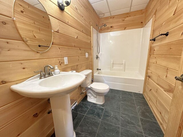bathroom with tub / shower combination, toilet, a paneled ceiling, and wooden walls