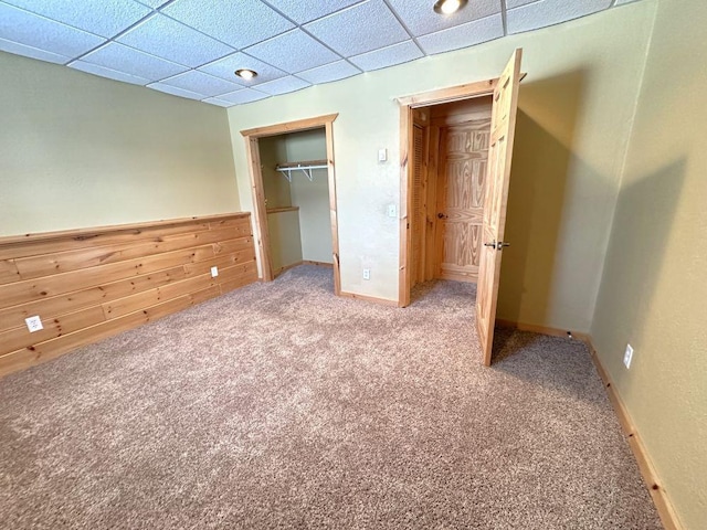 unfurnished bedroom featuring a wainscoted wall, a closet, carpet flooring, wooden walls, and a paneled ceiling