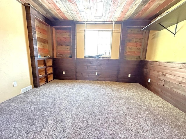 carpeted spare room featuring visible vents, wooden walls, and wooden ceiling