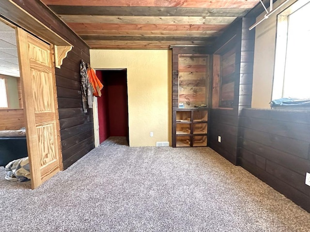 unfurnished bedroom with carpet floors, wood walls, and multiple windows