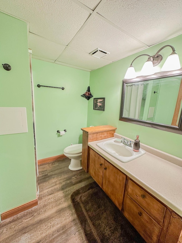 bathroom with hardwood / wood-style floors, vanity, a drop ceiling, and toilet