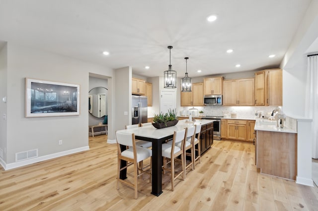 kitchen featuring appliances with stainless steel finishes, tasteful backsplash, decorative light fixtures, light wood-type flooring, and light brown cabinetry