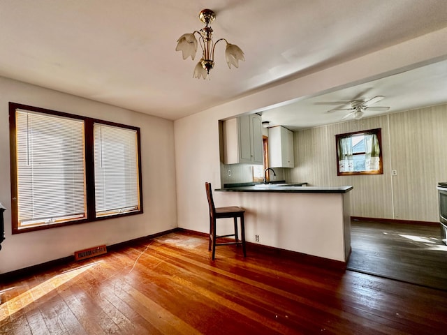 kitchen with hanging light fixtures, kitchen peninsula, ceiling fan, dark hardwood / wood-style flooring, and a breakfast bar