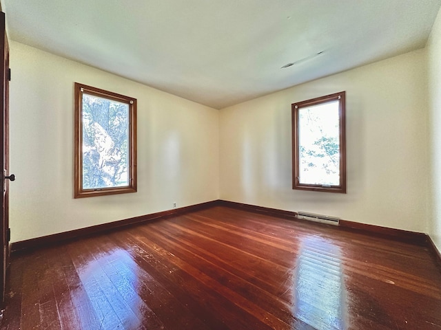 empty room featuring a baseboard radiator, dark hardwood / wood-style flooring, and plenty of natural light