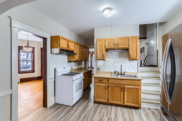 kitchen with sink, stainless steel refrigerator, white range with gas stovetop, decorative backsplash, and light wood-type flooring