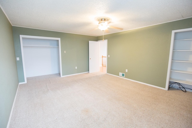 unfurnished bedroom with a textured ceiling, a closet, light colored carpet, and ceiling fan