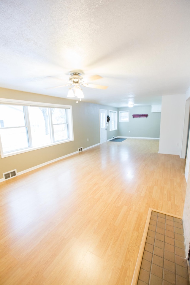 707 Haarfager Ave N, Canby, MN 56220 - unfurnished living room featuring ceiling fan, light wood-style floors, healthy amount of natural light, baseboards, and a textured ceiling