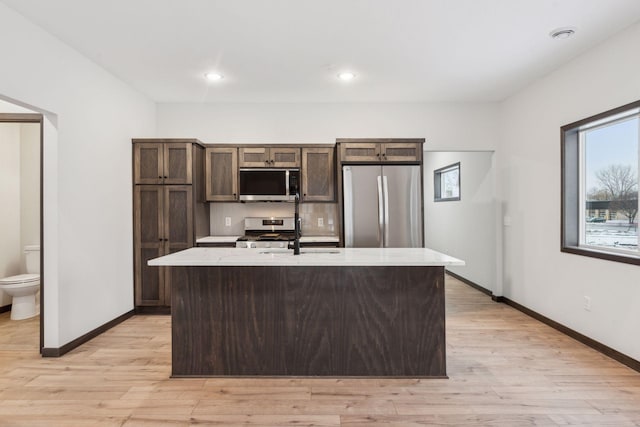 kitchen with sink, light wood-type flooring, a kitchen island with sink, and appliances with stainless steel finishes