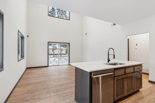 kitchen with light wood-type flooring, dark brown cabinets, sink, dishwasher, and an island with sink