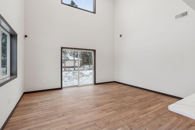 unfurnished living room featuring a high ceiling, light hardwood / wood-style floors, and a healthy amount of sunlight