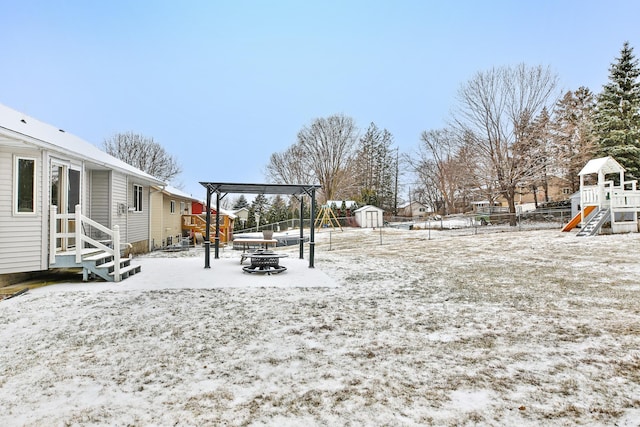 yard layered in snow with a playground, a fire pit, and a storage unit