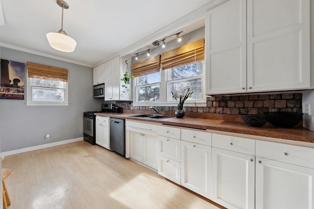 kitchen featuring butcher block counters, stainless steel appliances, decorative light fixtures, white cabinets, and sink