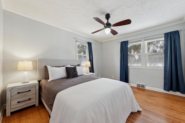 bedroom with ceiling fan, a textured ceiling, hardwood / wood-style flooring, and crown molding