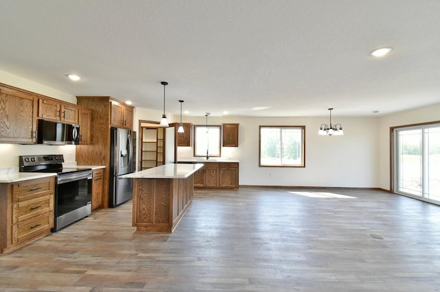 kitchen featuring light wood-type flooring, stainless steel appliances, decorative light fixtures, an inviting chandelier, and a center island