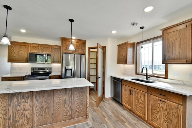 kitchen with pendant lighting, sink, light stone countertops, light hardwood / wood-style floors, and stainless steel appliances