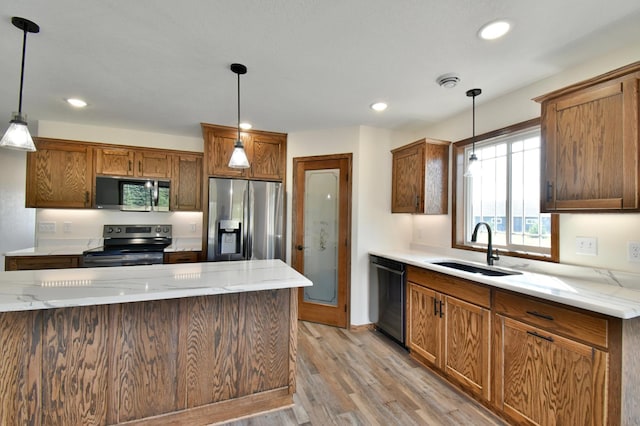 kitchen with light stone counters, stainless steel appliances, sink, decorative light fixtures, and light hardwood / wood-style floors