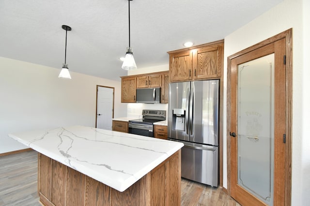 kitchen featuring light stone countertops, a center island, stainless steel appliances, pendant lighting, and light wood-type flooring