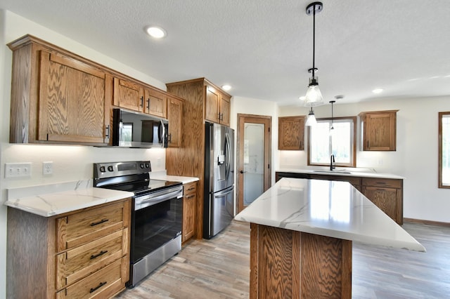 kitchen featuring sink, light hardwood / wood-style floors, pendant lighting, a kitchen island, and appliances with stainless steel finishes