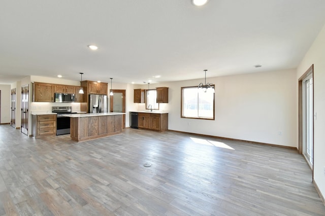 kitchen with light wood-type flooring, appliances with stainless steel finishes, decorative light fixtures, a kitchen island, and a chandelier