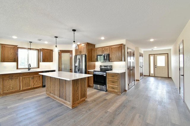 kitchen featuring a healthy amount of sunlight, sink, appliances with stainless steel finishes, decorative light fixtures, and a kitchen island