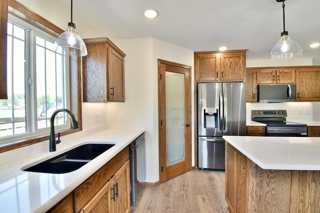 kitchen featuring sink, stainless steel appliances, decorative light fixtures, and light hardwood / wood-style floors