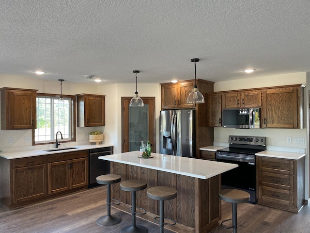 kitchen featuring a center island, sink, dark hardwood / wood-style floors, appliances with stainless steel finishes, and decorative light fixtures