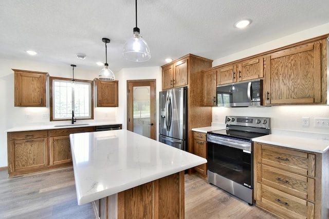 kitchen featuring a kitchen island, sink, stainless steel appliances, and hanging light fixtures