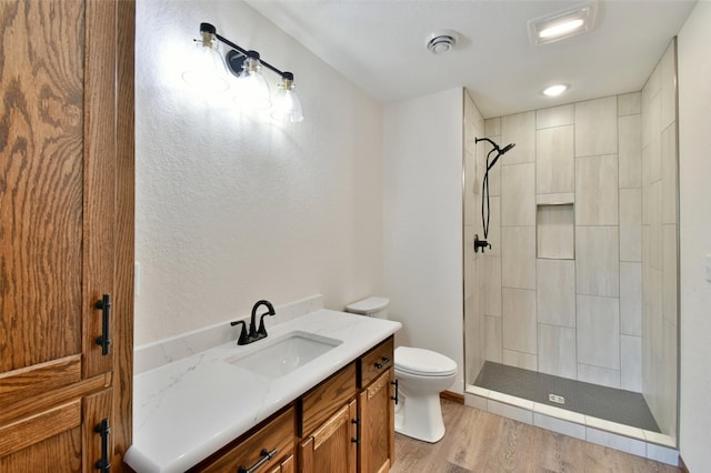 bathroom featuring hardwood / wood-style flooring, vanity, toilet, and a tile shower