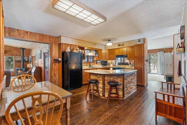 kitchen with a kitchen island, a breakfast bar, wood walls, sink, and black fridge